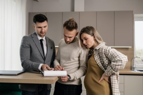 A pregnant woman and her husband talking to a real estate agent in the kitchen.