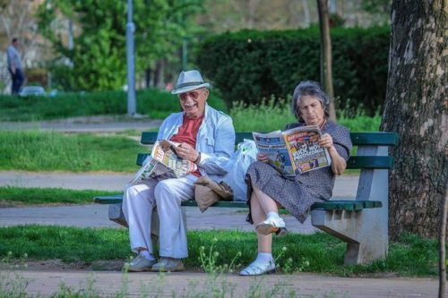 an old retired couple sitting on a bench in a park.