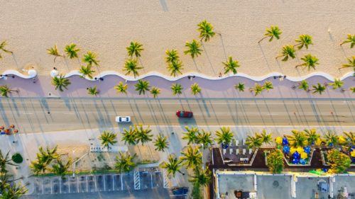 An aerial shot of a road next to the palm beach in Miami.