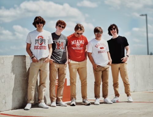 Five students wearing their university T-shirts standing next to each other, smiling and laughing.