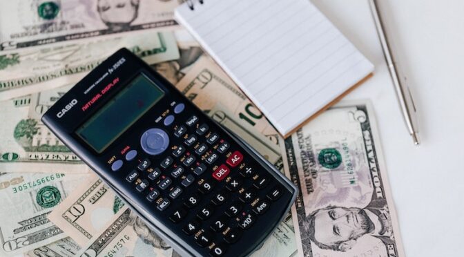 A calculator and a notepad on top of a pile of money