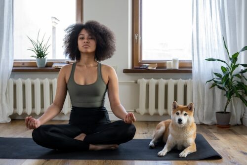 A girl sitting next to her dog and meditating.