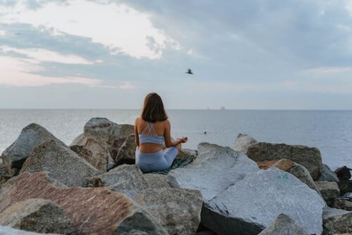 A woman in blue sportswear meditating on rocks near the sea