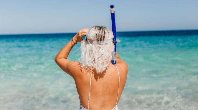 A woman with snorkeling equipment at the beach.