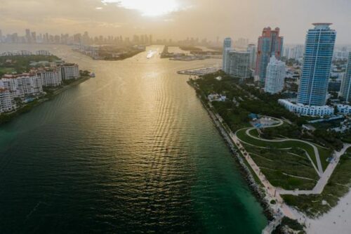 Aerial view of Miami with skyscrapers beside a waterfront, during sunset.