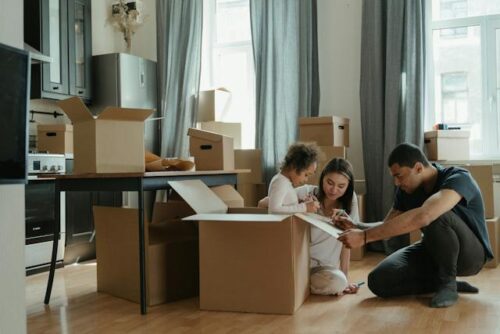 A family with a young child unpacking boxes in a room with sunlight streaming through the windows.