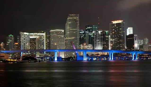 Night view of Miami's illuminated skyline with skyscrapers and the reflection on the water.