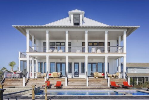 A luxurious two-story beach house with a pool and multiple balconies overlooking the ocean, reflecting an opulent lifestyle