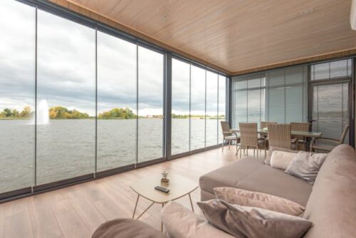 A spacious living room with floor-to-ceiling windows overlooking calm waters, embodying modern waterfront living.