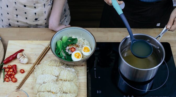 Two people cooking a bowl of ramen.